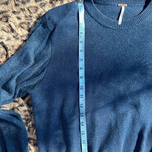 Puede incluir: Un su&eacute;ter azul oscuro con textura brillante. El su&eacute;ter tiene mangas largas y un cuello redondo. Una cinta m&eacute;trica se coloca a lo largo del lado del su&eacute;ter, mostrando una medida de 48 cm.