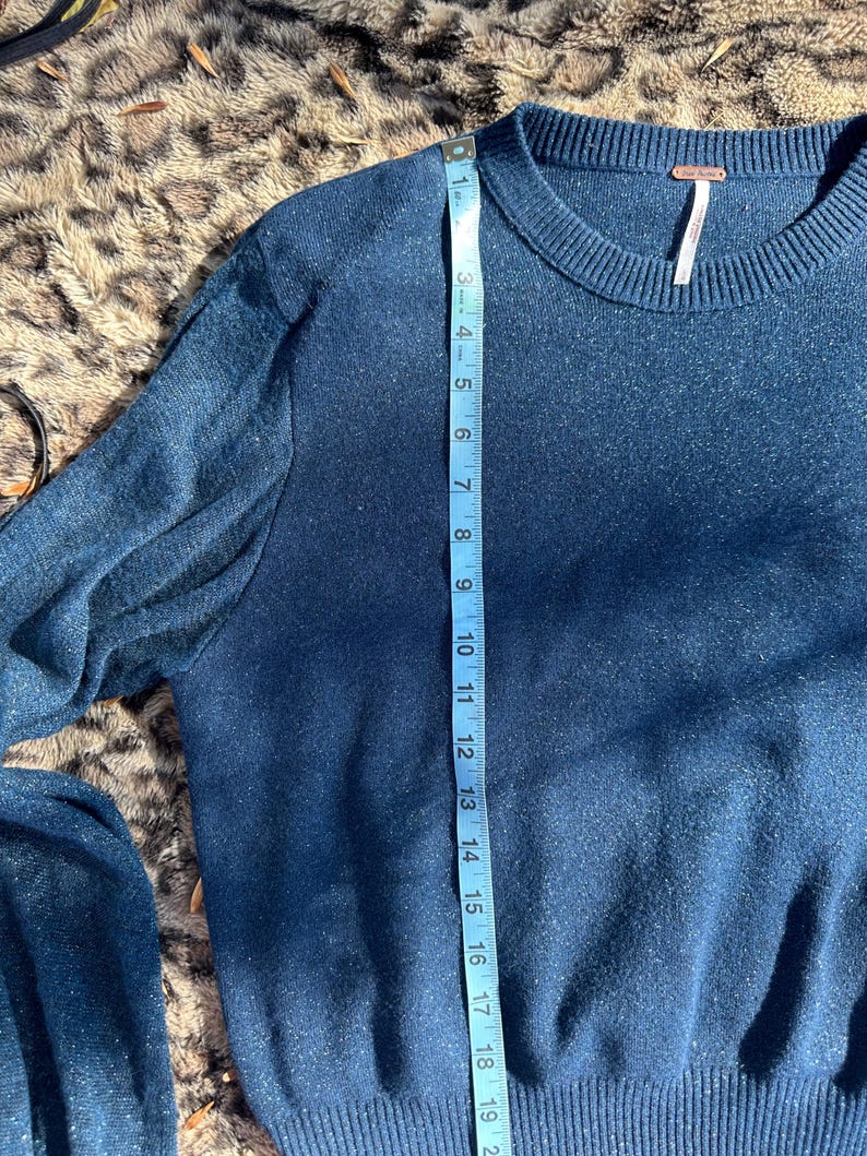 Puede incluir: Un su&eacute;ter azul oscuro con textura brillante. El su&eacute;ter tiene mangas largas y un cuello redondo. Una cinta m&eacute;trica se coloca a lo largo del lado del su&eacute;ter, mostrando una medida de 48 cm.