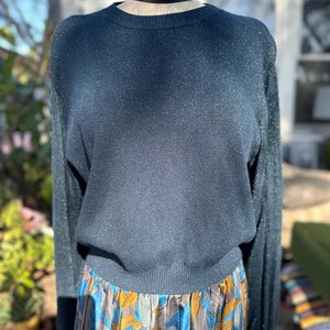 Puede incluir: Un su&eacute;ter azul oscuro con brillo, mangas largas y cuello redondo. El su&eacute;ter est&aacute; en un maniqu&iacute; y se combina con una falda estampada de colores.