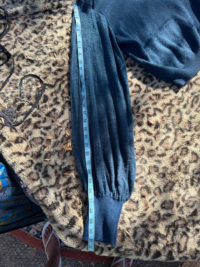 Puede incluir: Un su&eacute;ter azul oscuro con mangas largas y pu&ntilde;os de canal&eacute;. El su&eacute;ter se mide con una cinta m&eacute;trica, mostrando que la longitud de la manga es de 81 cm.