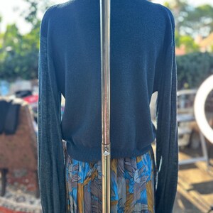 Puede incluir: Un su&eacute;ter azul teal de manga larga con dobladillo y pu&ntilde;os de canal&eacute;. El su&eacute;ter est&aacute; en un maniqu&iacute; y se combina con una falda estampada azul, dorada y blanca.