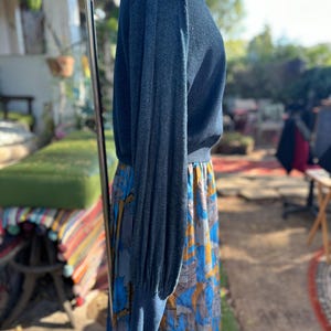 Puede incluir: Un su&eacute;ter azul de manga larga con textura acanalada y una silueta ligeramente ajustada. El su&eacute;ter se combina con una falda estampada de colores.