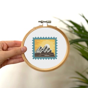 May include: A cross-stitch embroidery hoop featuring a blue and yellow stamp design with a stylised image of the Sydney Opera House.