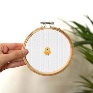 May include: A yellow pixelated chick cross-stitch pattern in a wooden embroidery hoop.