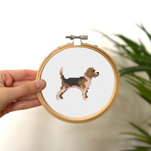 May include: A cross-stitch embroidery hoop with a brown, black, and white beagle dog design.