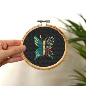 May include: A cross-stitch embroidery hoop with a black fabric background featuring a green and yellow butterfly with red and orange flowers on one side.