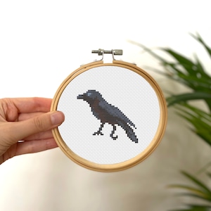 May include: A black crow cross-stitch pattern in a round wooden embroidery hoop.
