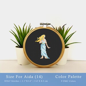 May include: Cross stitch pattern of a woman with long blonde hair wearing a light blue dress. The pattern is displayed in a wooden embroidery hoop on a white surface. The pattern is 30 by 47 stitches and measures 2.1 inches by 3.4 inches. The pattern uses 9 DMC colors.