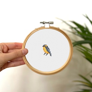 May include: A small, yellow and blue bird cross-stitch pattern in a wooden embroidery hoop.