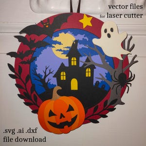 May include: A Halloween-themed wreath with a haunted house, bats, a ghost, and a jack-o'-lantern. The wreath is circular, with a red outer ring and a blue and purple background. The text "vector files for laser cutter" and ".svg .ai .dxf file download" are visible.