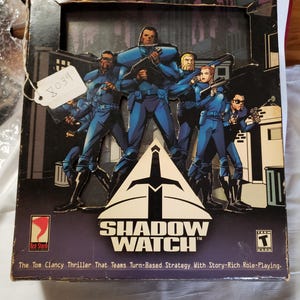 May include: A vintage Shadow Watch video game box. The box features a group of characters in blue uniforms holding weapons, set against a cityscape backdrop. The game's title is prominently displayed with the Red Storm logo.
