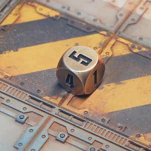 May include: A brass-colored, six-sided die with the number 5 visible. The die is set against a background of a metal surface with yellow and black stripes and the text "TOXIC INTAKE".