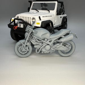 Peut inclure: Modèle de moto grise avec une selle noire et un modèle de Jeep Rubicon blanche en arrière-plan.