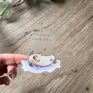 May include: A clear sticker with a cartoon pug lying on its back. The sticker has the text "I PUGGIN' LOVE YOU." printed on it.