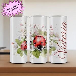 May include: Three white insulated tumblers with a ladybug and floral design. One tumbler has the name "Victoria" in a burgundy script. The tumblers are decorated with red ladybirds, white flowers, and green leaves. The text "6 FREE DESIGNS INCLUDED" is in a pink starburst.