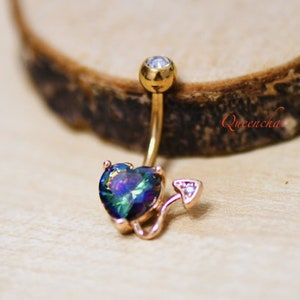 May include: Gold belly button ring with a rainbow heart and a small tail. The heart has a clear gem in the center.