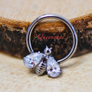 May include: A silver body jewellery ring with a clear crystal bee charm. The ring is made of surgical steel and is suitable for a variety of piercings.