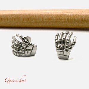 May include: A pair of silver skeleton hand earrings. The earrings are made of metal and feature a detailed design.