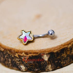May include: A silver belly button ring with a gold star charm featuring an iridescent gem in the centre.