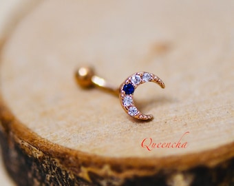 May include: A gold crescent moon body jewelry with a blue gemstone and clear rhinestones.