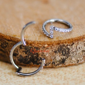 May include: Two silver hoop earrings with small clear gemstones. One hoop is a simple circle, the other is a curved line with gemstones.