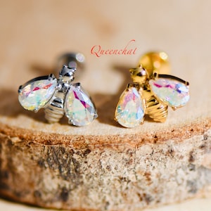 May include: Two bee-shaped earrings with iridescent teardrop-shaped crystals. The earrings are available in silver and gold.
