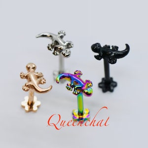 May include: Four different coloured gecko-shaped body jewellery pieces. The geckos are made of metal and have a shiny finish. The colours are silver, gold, black, and rainbow.