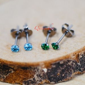 May include: Three pairs of stud earrings with small gemstone accents. The earrings are silver in colour and have a post back. The gemstones are blue and green.