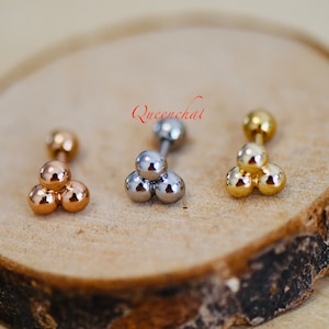 May include: Three different coloured triple ball barbell earrings. The earrings are made of surgical steel and are available in gold, silver, and rose gold.