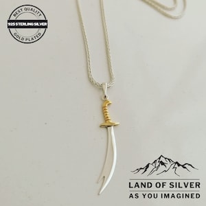 May include: A silver necklace with a gold-plated sword pendant. The necklace is on a white background. The pendant is a stylized sword with a curved blade. The necklace is labeled "Best Quality 925 Sterling Silver Gold Plated".
