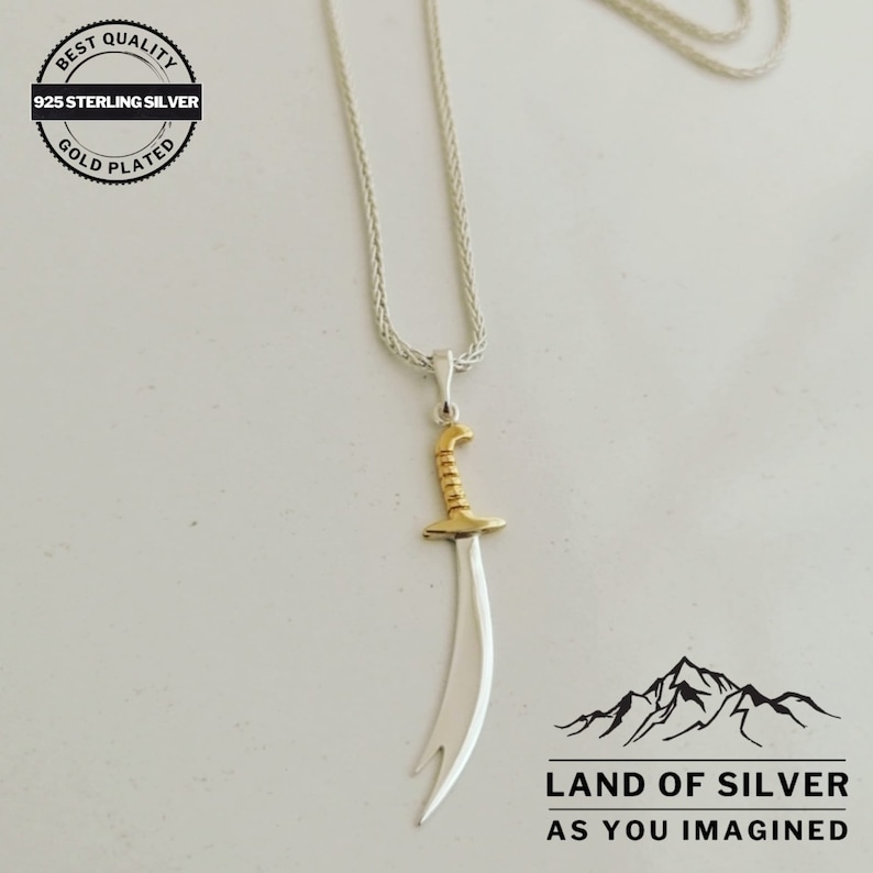 May include: A silver necklace with a gold-plated sword pendant. The necklace is on a white background. The pendant is a stylized sword with a curved blade. The necklace is labeled "Best Quality 925 Sterling Silver Gold Plated".