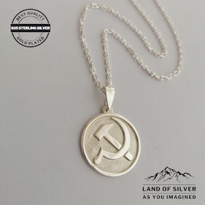 May include: Silver necklace with a round pendant featuring a hammer and sickle symbol. The pendant is gold plated and has a textured surface. The necklace is 925 sterling silver and is labeled "Best Quality Gold Plated 925 Sterling Silver".