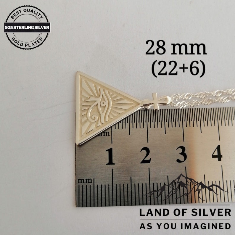 May include: Silver pendant necklace featuring a triangle with an eye inside and a cross charm. The pendant measures 28 mm (22+6).