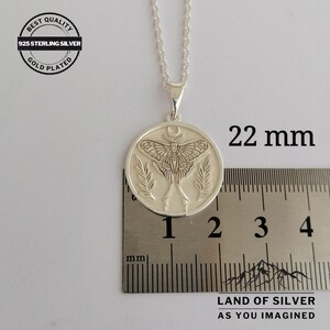 May include: A silver pendant necklace with a detailed moth design, measuring 2.2 cm in diameter. The pendant features a moth with intricate wing patterns, a crescent moon, and leaf accents. The necklace is labeled "925 Sterling Silver" and "Gold Plated".