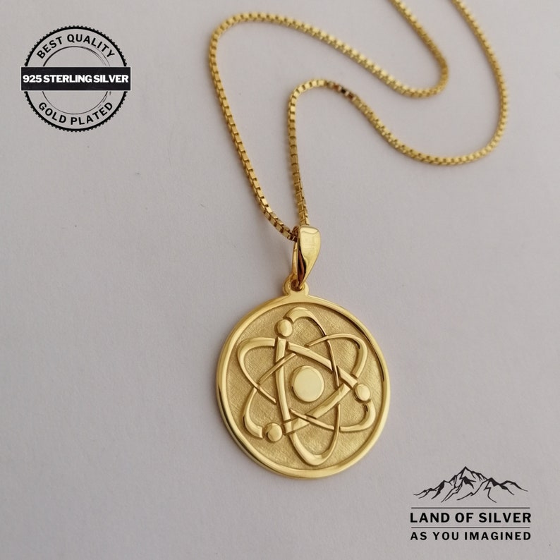 May include: Gold plated 925 sterling silver necklace with an atom pendant. The pendant is a round disc with a raised atom design. The chain is a box chain.