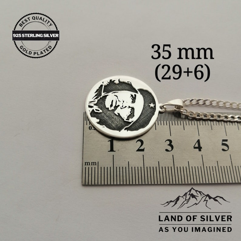 May include: A silver pendant with a black and white image of a man's face. The pendant is 35 mm in diameter and is on a silver chain. The pendant is labeled "925 Sterling Silver" and "Gold Plated".