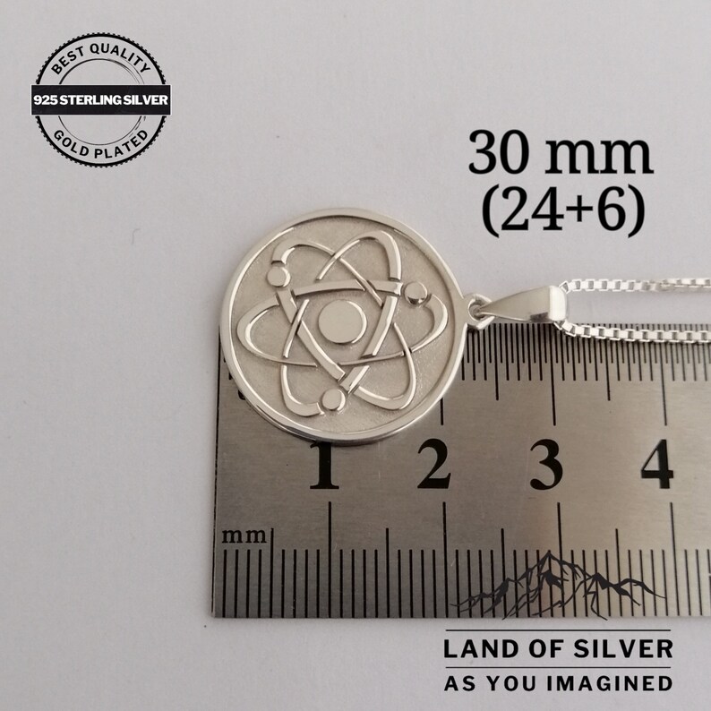 May include: Silver atom pendant necklace with a 30 mm diameter. The pendant is made of 925 sterling silver and is gold plated. The pendant is shown on a ruler with the text "LAND OF SILVER AS YOU IMAGINED".