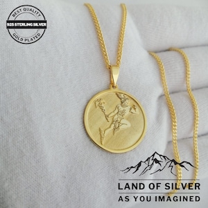 May include: Gold-plated 925 sterling silver necklace with a round pendant featuring a detailed engraving of a winged figure holding a staff. The pendant is attached to a delicate chain.