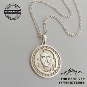 May include: Silver necklace with a round pendant featuring a profile portrait of a man with a beard and a star-shaped border. The pendant is on a silver chain.