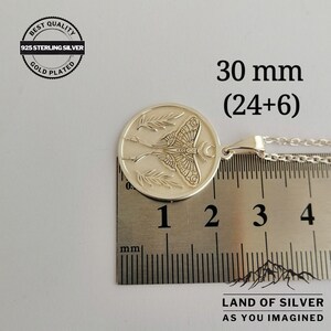 May include: A silver pendant necklace featuring a moth design, measuring 30 mm. The round pendant has a detailed moth and leaf design. The text "BEST QUALITY 925 STERLING SILVER GOLD PLATED" is in a circle on the upper left. The text "LAND OF SILVER AS YOU IMAGINED" is at the bottom.