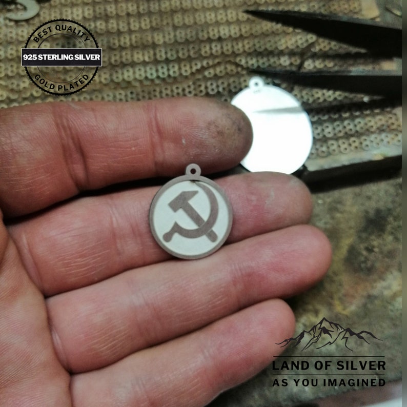 May include: A silver pendant with a gold-plated finish featuring a red hammer and sickle symbol on a white background. The pendant is 925 sterling silver and is labeled "Best Quality" and "Gold Plated".