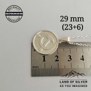May include: Silver pendant necklace featuring a hammer and sickle symbol on a round disc. The pendant measures 29 mm (23 mm + 6 mm) in diameter. The necklace is made of 925 sterling silver and is gold plated.
