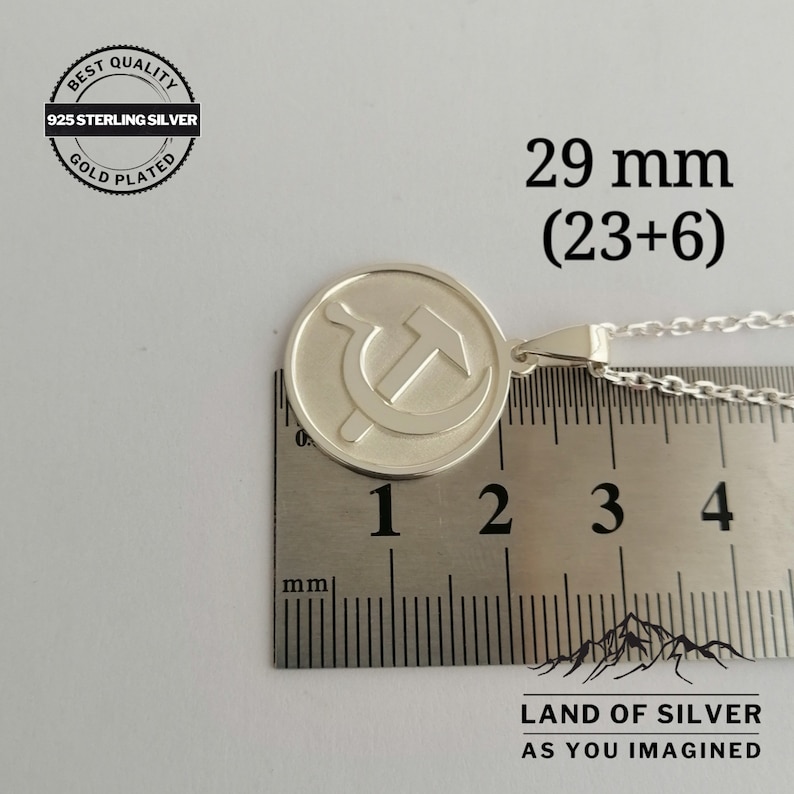 May include: Silver pendant necklace featuring a hammer and sickle symbol on a round disc. The pendant measures 29 mm (23 mm + 6 mm) in diameter. The necklace is made of 925 sterling silver and is gold plated.