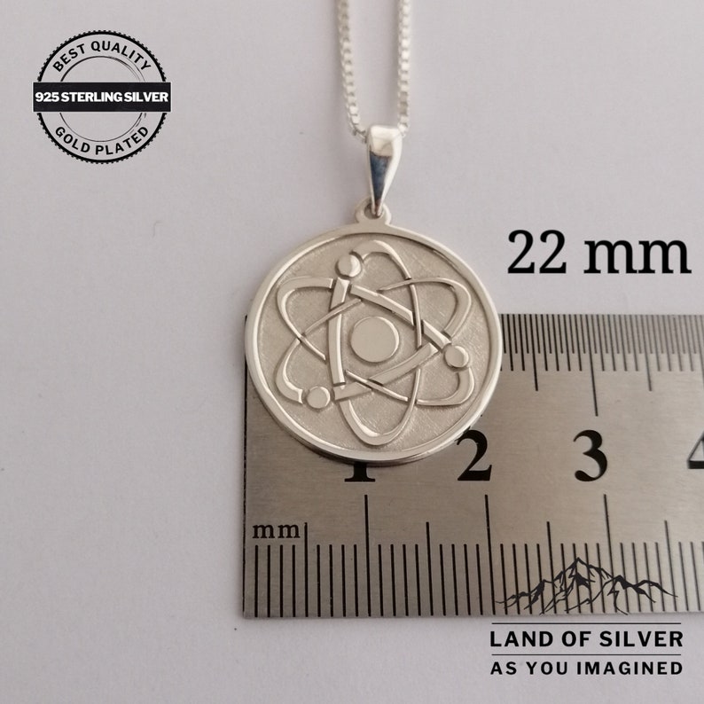 May include: Silver necklace with a 22 mm round pendant featuring a detailed atom design. The pendant is made of 925 sterling silver and is gold plated. The necklace is 22 mm in diameter.