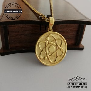 May include: Gold plated 925 sterling silver necklace with an atom pendant. The pendant is round and features a detailed atom design. The necklace is displayed on a wooden box with the words "Best Quality" and "Gold Plated" on a tag.