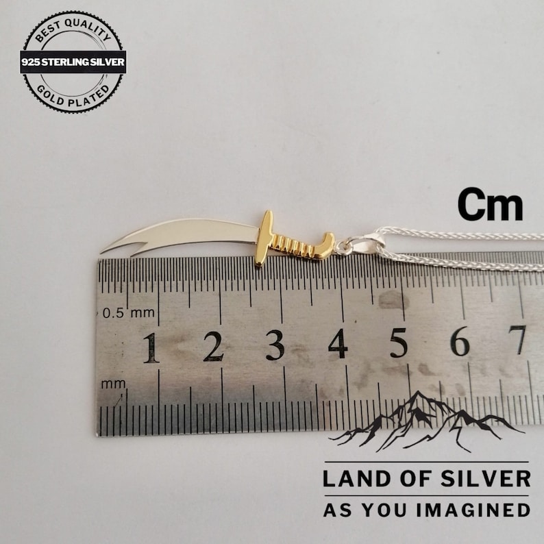 May include: A silver and gold pendant in the shape of a scimitar sword, measuring 4 cm in length, on a silver chain. The pendant is made of 925 sterling silver and is gold plated. The image includes the text "BEST QUALITY 925 STERLING SILVER GOLD PLATED" and "LAND OF SILVER AS YOU IMAGINED".