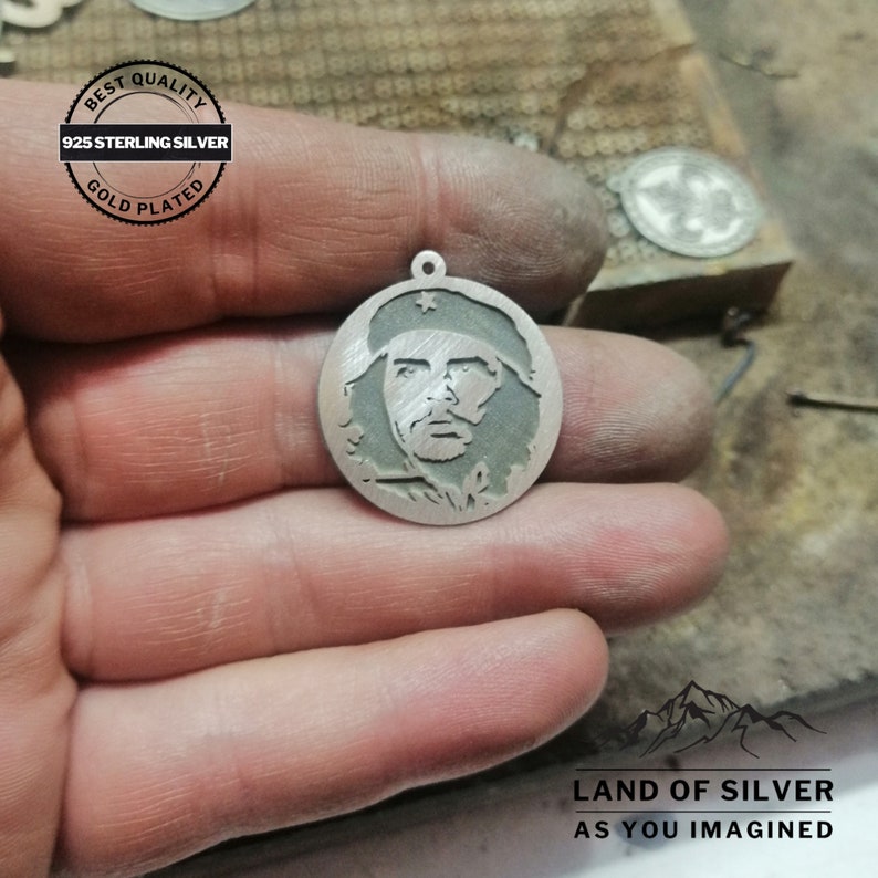 May include: Silver pendant featuring a detailed profile of Che Guevara, a famous revolutionary figure. The pendant is round and has a gold-plated finish. The text "925 Sterling Silver" and "Best Quality Gold Plated" is visible on the image.