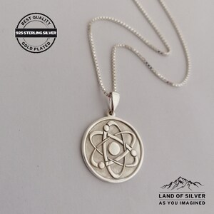 May include: A silver necklace with a round pendant featuring a stylized atom design. The pendant is gold plated and the chain is a box chain. The necklace is labeled "925 Sterling Silver" and "Gold Plated".