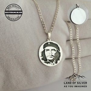 May include: A silver chain necklace with a round pendant featuring a black and white silhouette of Che Guevara. The pendant is engraved with a star and the text "925". The chain is a curb chain style. The necklace is on a white background.