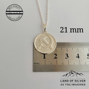 May include: Silver pendant necklace featuring a 21 mm round charm with a hammer and sickle design. The charm is gold plated and has the text "BEST QUALITY 925 STERLING SILVER GOLD PLATED" on the back. The necklace is on a silver chain.